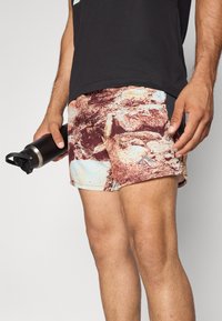 Schwimmshorts mit einem mehrfarbigen, felsigen Muster aus einem weichen, leichten Stoff. Seitentasche und ein kontrastierendes Material am Saum.