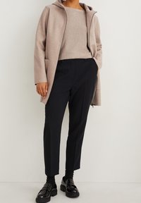 Abrigo capucha color beige claro sobre una blusa beige, combinado con pantalones negros ajustados y mocasines negros brillantes. Texturas suaves y diseño minimalista.