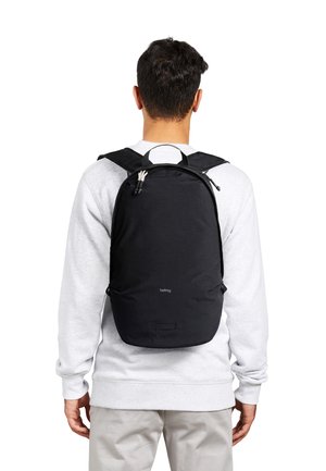 Mann trägt hellgraues Sweatshirt und Hose, trägt einen schwarzen Bellroy-Rucksack, von hinten vor weißem Hintergrund gesehen.