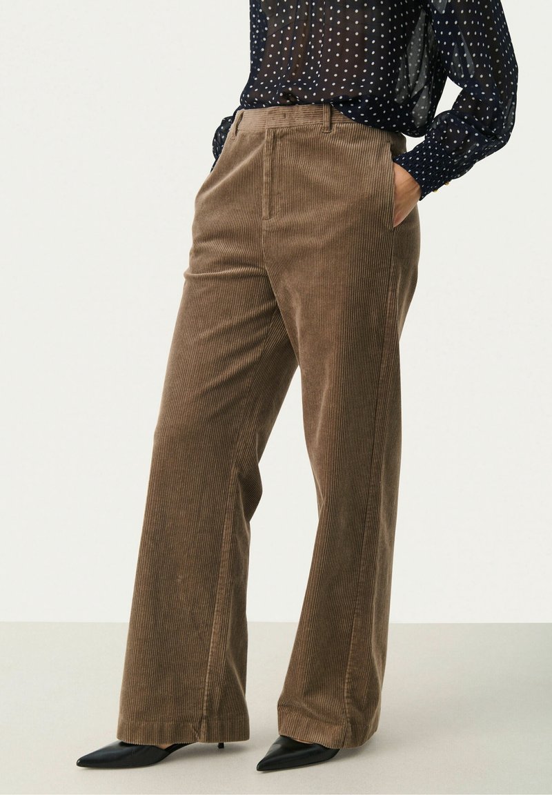 Pantalon large en velours côtelé marron porté avec un chemisier transparent bleu marine à pois blancs et des talons noirs pointus.