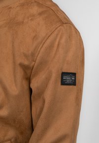 Giacca in suede marrone con finitura testurizzata, design aderente e un patch logo nero sulla manica sinistra.