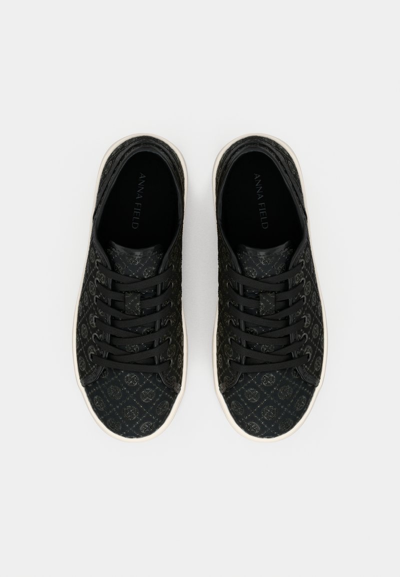 Schwarze Sneakers mit Muster, flachen Schnürsenkeln und einer strukturierten Oberfläche. Sie haben eine weiße Sohle und ein Logo auf der Innensohle.
