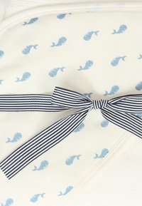 Coperta per bambini in cotone con una base crema caratterizzata da piccoli modelli di balene blu, fissata con un fiocco a righe blu e bianche.
