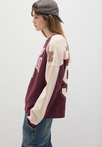 Bordeauxrood en beige sweatshirt met lange mouwen, voorzien van een grote cijferprint op de achterkant en tekst aan de voorkant. Van zacht katoen.