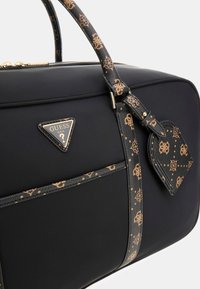 Sac à main noir avec quincaillerie dorée. Doté d'une sangle texturée avec un motif et d'une plaque logo triangulaire. Extérieur lisse avec fermeture éclair.