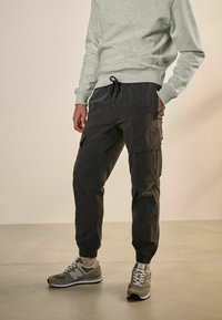 Grauer Sweatshirt und dunkle Cargo-Hosen mit elastischen Bündchen und mehreren Taschen, kombiniert mit grauen Sneakers. Glatte Textur, lässiges Design.