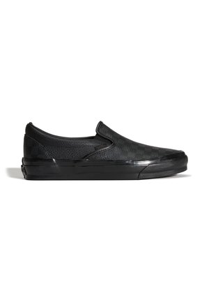 Sort slip-on sneaker med tekstureret læderoverdel og tyk gummisål, vist i profil på hvid baggrund.