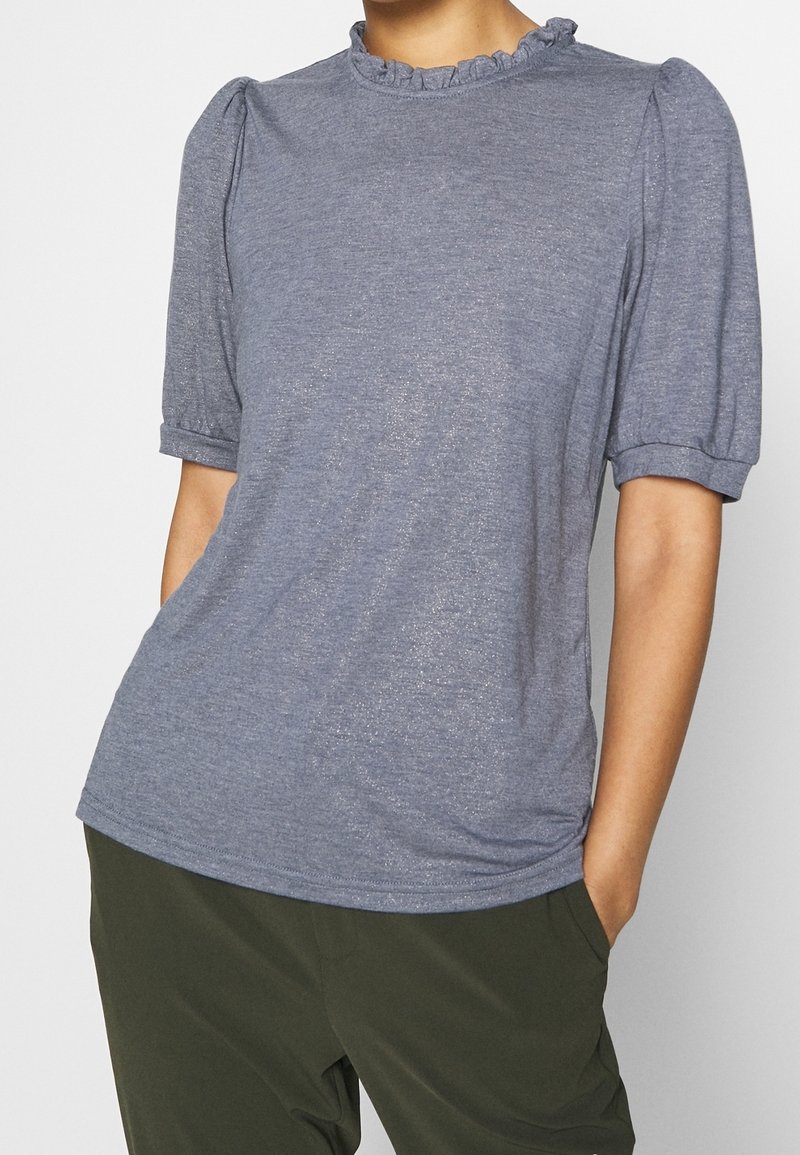 Camiseta de manga corta, de color azul claro, hecha de un tejido suave, con un escote con volantes y mangas fruncidas. Textura suave, corte casual.