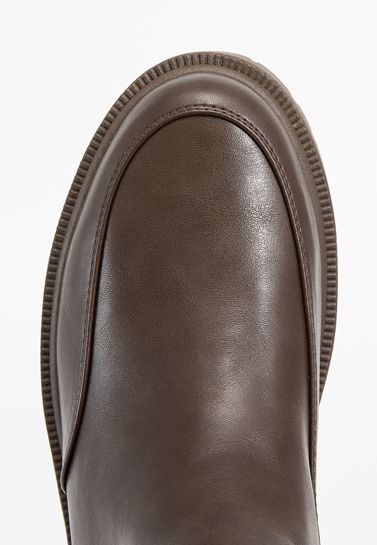Bottine en cuir marron avec une texture lisse, bout arrondi et détails côtelés le long de la semelle. Design minimaliste sans ornements.