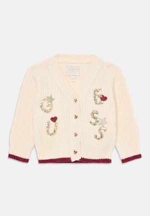 Kremowy sweter rozpinany z dzianiny z bordowymi lamówkami, guzikami w kształcie serca oraz złotymi cekinowymi literami tworzącymi napis "GUESS" z akcentami w postaci gwiazdek i serc.