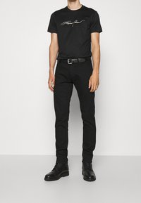 Black cotton t-shirt with a white script logo, paired with black pants and black lace-up boots. Straight leg design, no visible patterns.