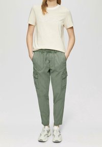 Světle pruhované tričko s textem "shine", spárované se zelenými cargo kalhotami s kapsami a stahovací šňůrkou v pase, obuté s šedými teniskami.