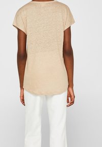 Top beige a maniche corte con una vestibilità rilassata, dotato di un collo rotondo e un orlo leggermente curvo, realizzato in un tessuto leggero e testurizzato.