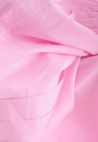 Tissu rose clair avec une texture lisse présentant des détails pliés et des coutures subtiles, créant des volumes et des vagues douces.