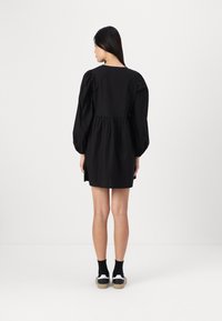 Vestido preto com mangas bufantes, costura na cintura e saia evasê. A modelo usa ténis brancos com detalhes em preto e meias cano curto pretas.