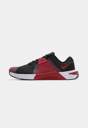Baskets de sport noires et rouges avec une tige en mesh texturé, arborant un logo Nike proéminent et une semelle intermédiaire blanche avec une semelle extérieure en caoutchouc à motifs.