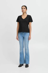 T-shirt nera a maniche corte con scollatura a V abbinata a jeans svasati di colore blu chiaro. Il modello indossa stivaletti neri con tacco. Design semplice, vestibilità casual.