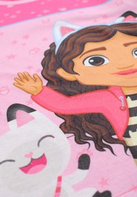 T-shirt en coton arborant un personnage de dessin animé aux cheveux bouclés et veste rose, accompagné d'un chat blanc souriant, sur un fond rose avec des étoiles.