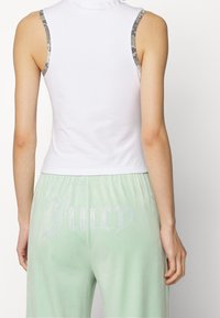 Bílý bezrukávový top se stříbrným hadím potiskem na ramenech; mátově zelené tepláky s nápisem "Juicy" zdobeným kamínky na zadní straně.