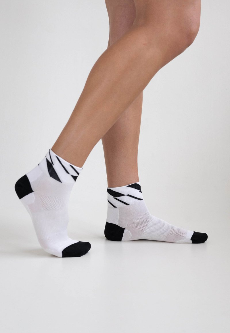Weiße Knöchelsocken mit schwarzen Akzenten und geometrischem Muster; aus einem strukturierten Material gefertigt, mit verstärktem Fersen- und Zehenbereich.