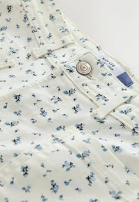 Ruime, cropped broek in crème met een bloemenpatroon in blauw en zwart. Voorzien van een metalen knoop en een label van stof met de naam van de collectie.