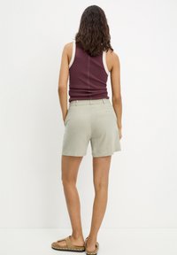 Strój damski składający się z bordowego topu na ramiączkach z kremową lamówką oraz zielonych krótkich spodenek z tylną kieszenią, wykonany z lekkiego materiału.