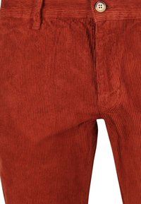 Roestkleurige corduroypanen met verticale ribbels en een enkele lichtbruine knoop op de tailleband, close-up van de voorkleur.