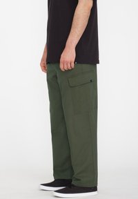 Groene katoenen cargo broek met zijzakken, relaxed fit en gestikte accenten, gecombineerd met zwarte schoenen en een zwart t-shirt.