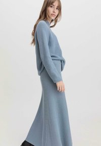 Himmelblauer Strick-Zweiteiler, bestehend aus einem Langarmoberteil und einem bodenlangen Rock, beide mit Rippstruktur und lockerer Passform.