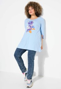 Tunika a maniche lunghe di colore azzurro chiaro con stampa grafica floreale. Abbinata a jeans slim fit e sneakers multicolori.