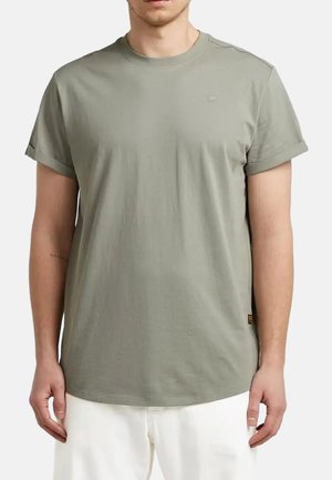 Uomo che indossa una maglietta verde chiaro a maniche corte con risvolti e pantaloni bianchi, mostrato dalle spalle alla vita.