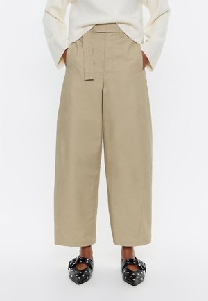 Beige bredbenede cropped bukser med fastgjort bælte båret med hvid sweater og sorte spidse sko med nitter.