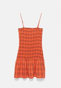 Robe orange sans manches avec fines bretelles et motif texturé, présentant un ourlet à volants et des lignes écossaises noires.