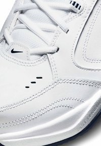 Vitt sportskor med slät läderöversida, meshinlägg, svart sömnad och logotyp på tungan samt en dämpad sula.