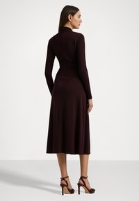 Burgundy långärmad klänning med figurnära överdel och utsvängd kjol, tillverkad av mjukt tyg, med hög halsringning och minimalt detaljerad.