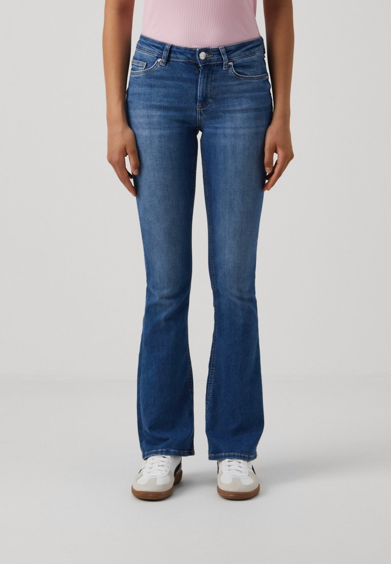 Räknade blå jeans i denim med hög midja, framfickor och en subtil tvätt. Kombinerat med vita sneakers.