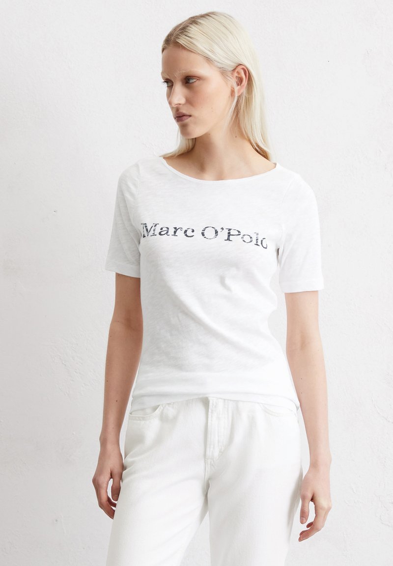 Kortærmet hvid T-shirt med rund halsudskæring, med "Marc O'Polo" trykt i mørkegrå. Blødt, struktureret stof, afslappet pasform.