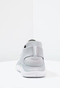 Szare sportowe buty z materiału, z wyściełanym piętem, elastycznymi paskami i białą gumową podeszwą z wytłoczonym napisem "NIKE FREE" na pięcie.
