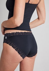 Ciemnoniebieskie majtki z koronkowym wykończeniem wokół pasa. Tkanina jest gładka, a krój dopasowany.