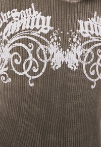 Brown ribbed fabric featuring white graphic text and ornate swirls. Design includes intricate patterns and a textured surface.