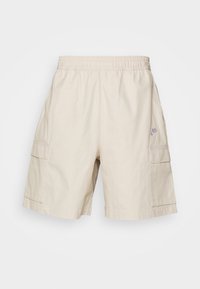 Béžové cargo šortky s elastickým pasem, dvěma bočními kapsami, náprsní kapsou na noze a logem Nike vpředu.