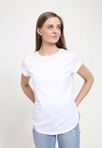 Hvid bomulds T-shirt med korte ærmer, rund hals og en tætsiddende pasform, parret med lyse denim jeans. Glat tekstur, minimalistisk stil.