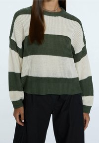 Knitted sweater featuring green and cream horizontal stripes, crew neckline, and ribbed cuffs with a relaxed fit. Fabric appears textured.