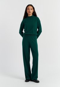 Groene gebreide trui en bijpassende broek, met een hoge halslijn, een relaxte pasvorm en een zachte textuur. Minimaal beslag en subtiele stiksels.