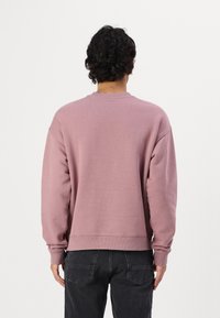 Mauve színű pulóver kapucnis felső, hosszú ujjal és kerek nyakkivágással. Bordás mandzsetták és tónusos szegély, az anyag lágy megjelenésű, bolyhos textúrával.