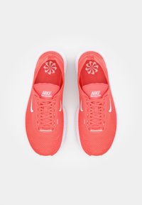 Nike Free juoksukengät, kirkas korallinvärinen verkkomateriaali, valkoiset yksityiskohdat, teksturoitu pohja, pyöreät nauhat, logo kengän kielessä ja pohjissa.