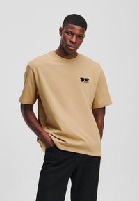 Tum lühikeste varrukatega T-särgid, mis on valmistatud puuvillast, mustade päikeseprillide graafika ja "KARL LAGERFELD" tekstiga vasakul rinnal.