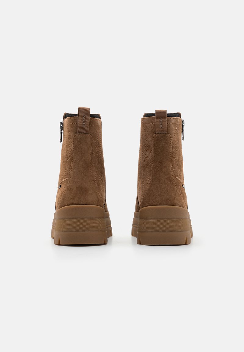 Botas de tobillo de ante marrón con suela de goma plana, que cuentan con un cierre lateral de cremallera y una lengüeta trasera cosida. Diseño simple y moderno.