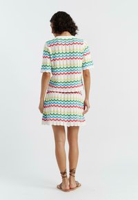 Gebreid twee-delig outfit met een structuurdesign en zigzagpatronen in rood, groen en blauw tegen een witte achtergrond. Korte mouwen en een uitlopende rok.