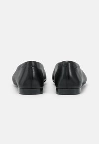 Paire de chaussures slip-on en cuir noir vues de dos sur un fond blanc uni.